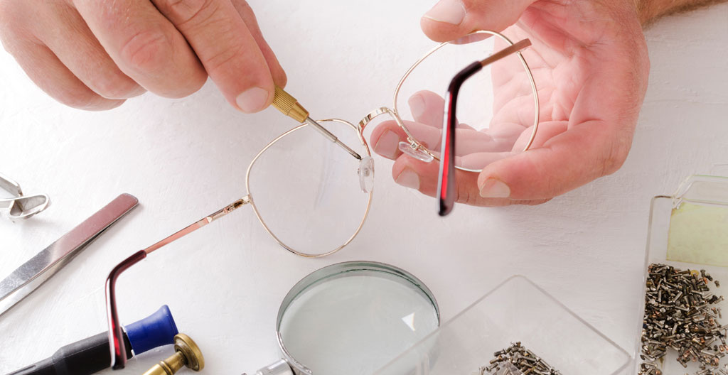 Les mains d'un opticien ajustent délicatement les branches d'une paire de lunettes sur un établi garni de petits outils